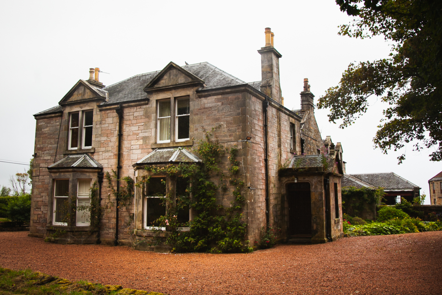 Kinkell House Large Farmhouse, with trailing rose bushes at the front and greenery around the house, red gravel on the roads